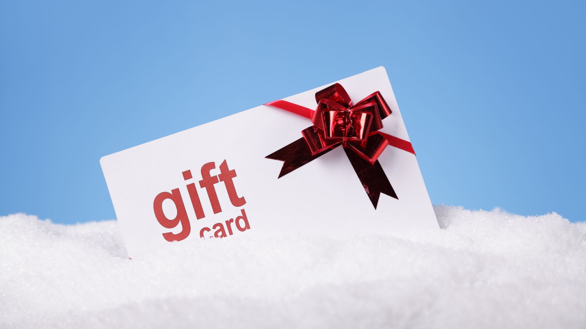 A gift card in the snow with a red bow.